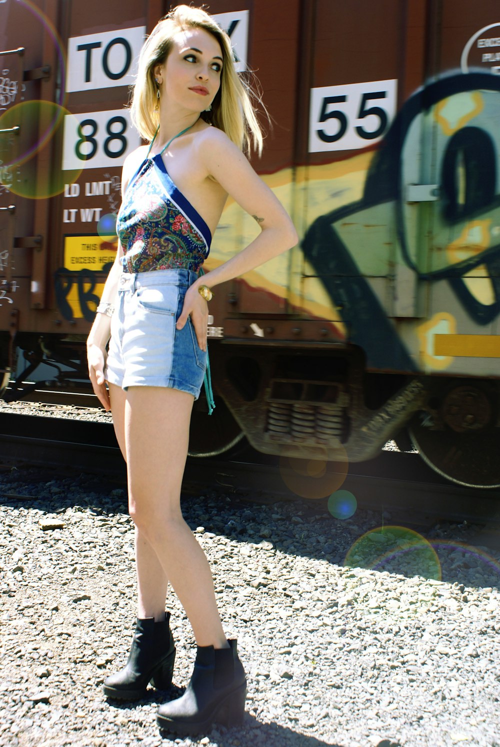Mujer con camiseta sin mangas floral azul y blanca y pantalones cortos de mezclilla azules de pie en la barandilla del tren