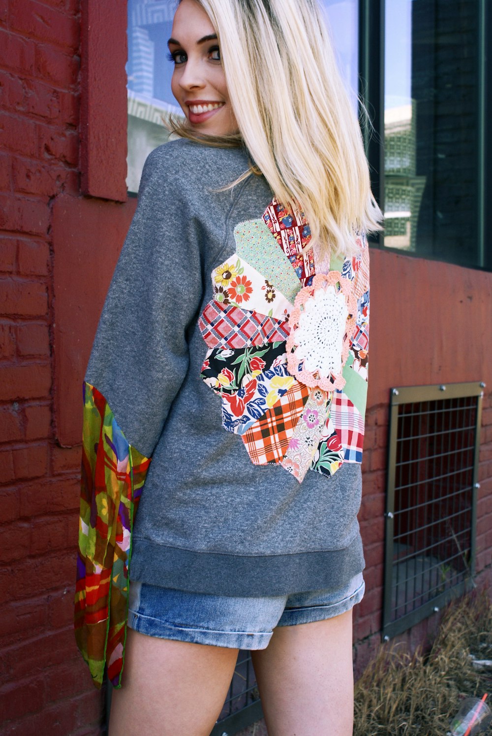 woman in gray sweater standing near brown brick wall