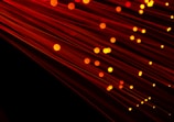 Numerous strands of glowing red-orange fiber optic cables create a dynamic and futuristic visual. The bright points of light accentuate the flowing lines against a dark background, giving a sense of motion.