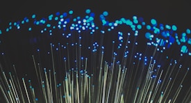 Clusters of blue lights on the tips of fiber optic cables create a captivating visual of glowing dots against a dark background.