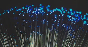 Clusters of blue lights on the tips of fiber optic cables create a captivating visual of glowing dots against a dark background.