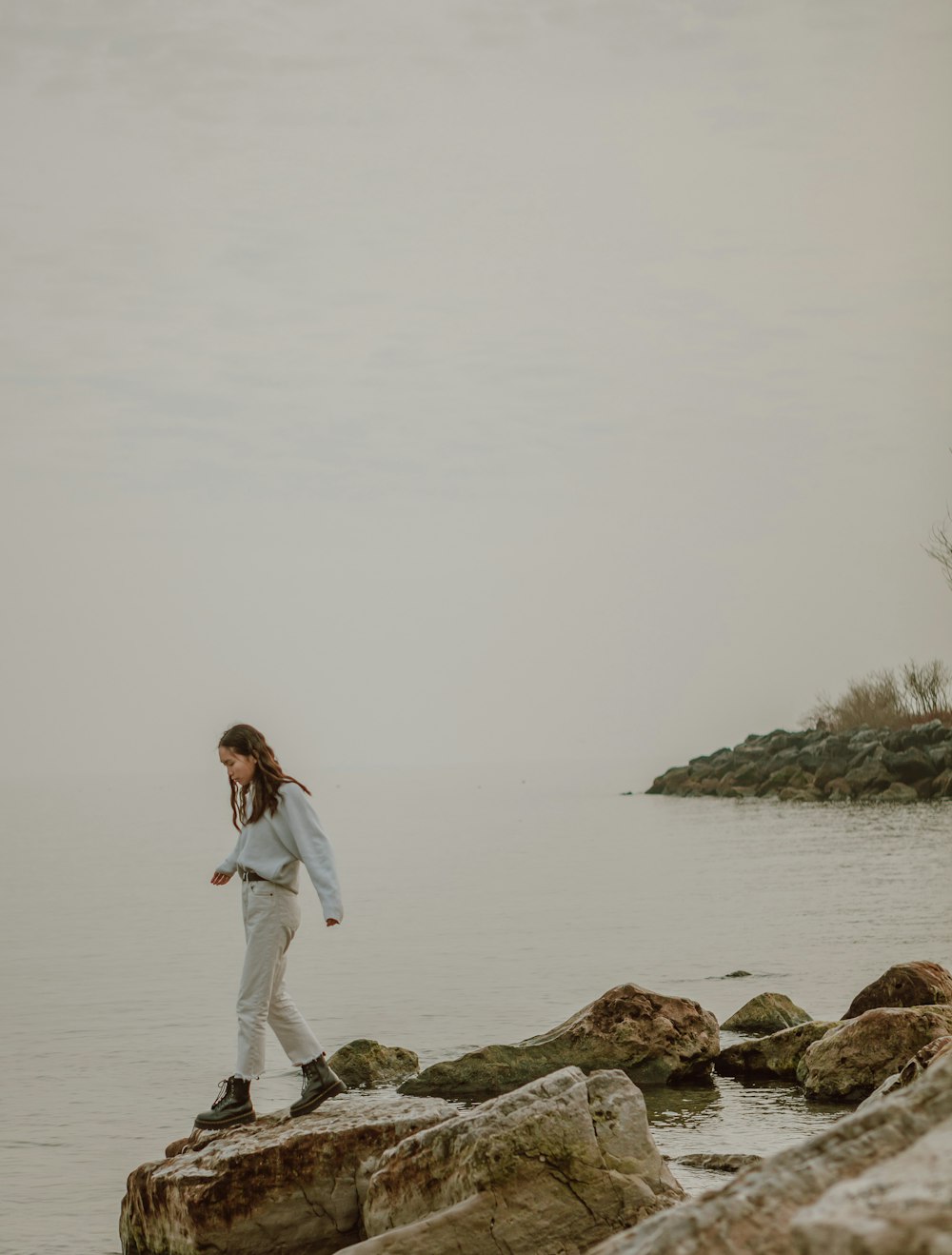 woman in white jacket standing on rock near body of water during daytime