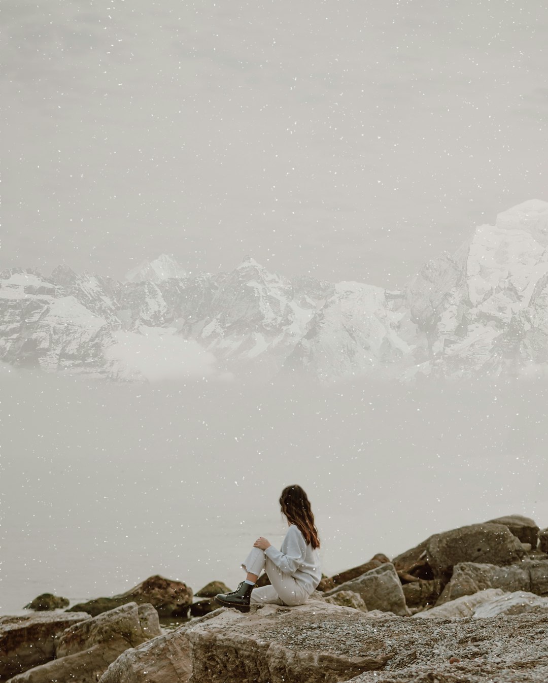woman in white shirt sitting on rock near snow covered mountain during daytime