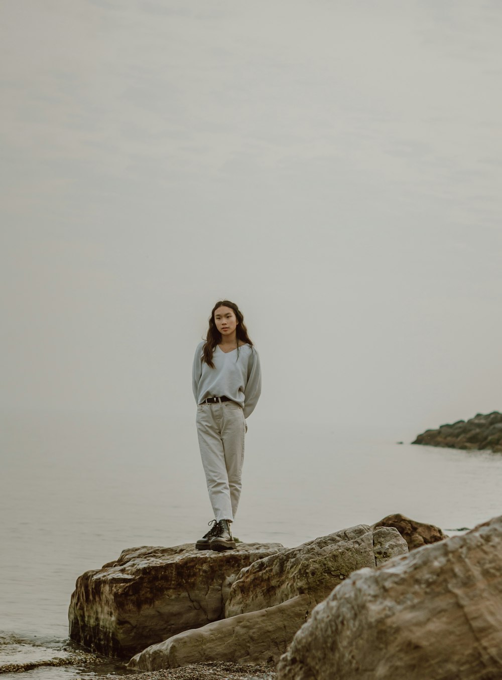 woman in white long sleeve shirt and white pants standing on brown rock near body of on on on on