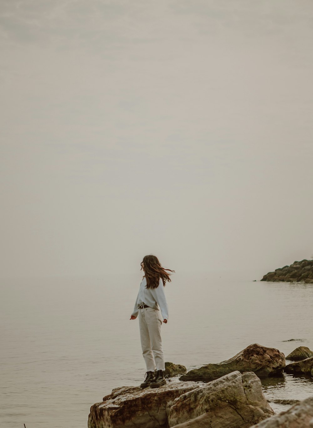 白い長袖シャツと白いズボンを着た女性が、オンオンの体の近くに茶色の岩の上に立っています