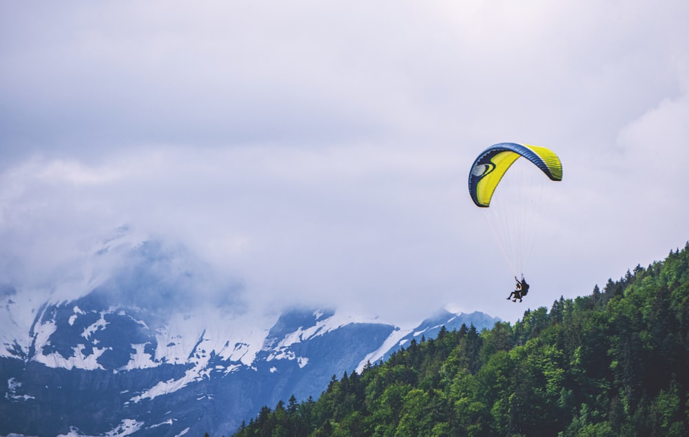 person riding yellow parachute over green trees and mountains during daytime