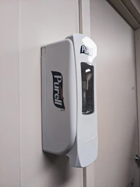 Close-up of a hand sanitizer dispenser mounted on a clean white wall.