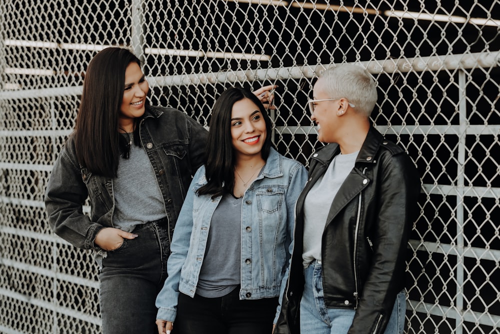 3 women standing beside gray metal fence