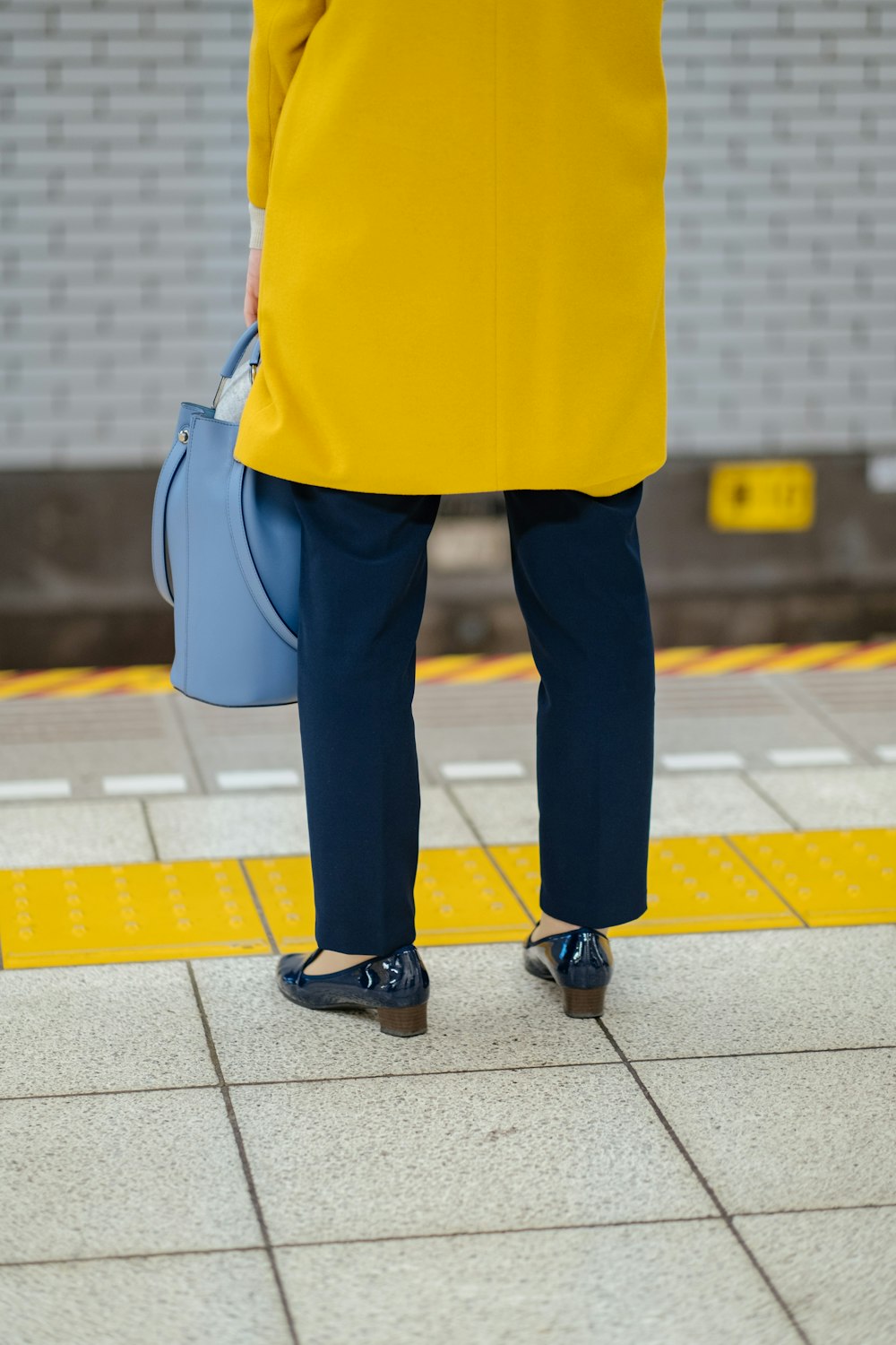 woman in yellow coat and black pants with blue leather sling bag