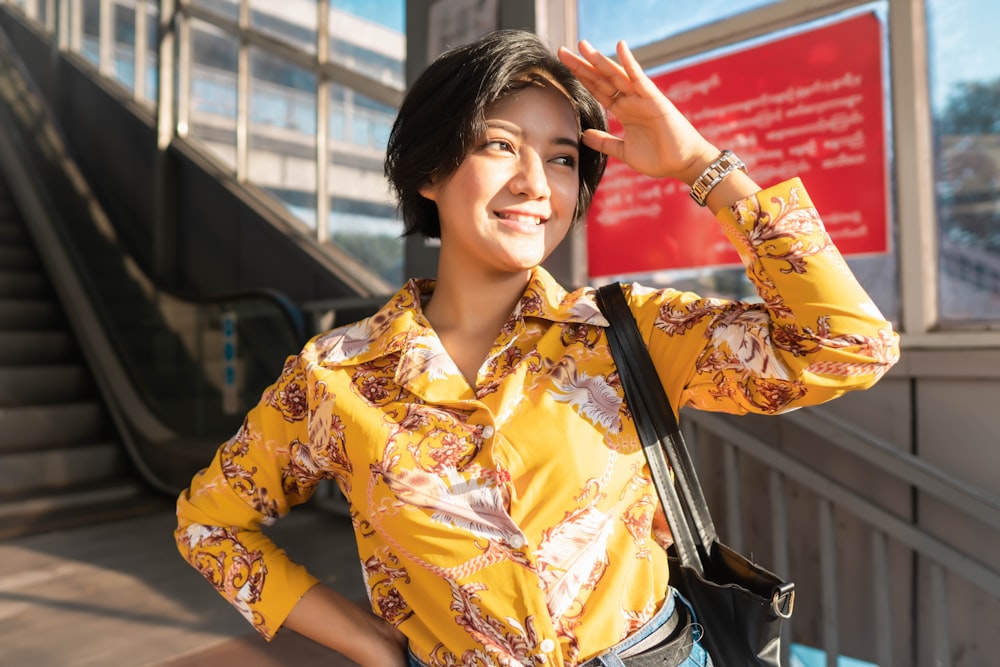 woman in yellow and white floral button up shirt holding her hair
