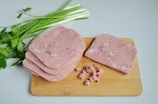Slices of sujuk and salami laid out on a wooden cutting board with a sprig of fenugreek.