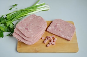 Slices of sujuk and salami laid out on a wooden cutting board with a sprig of fenugreek.