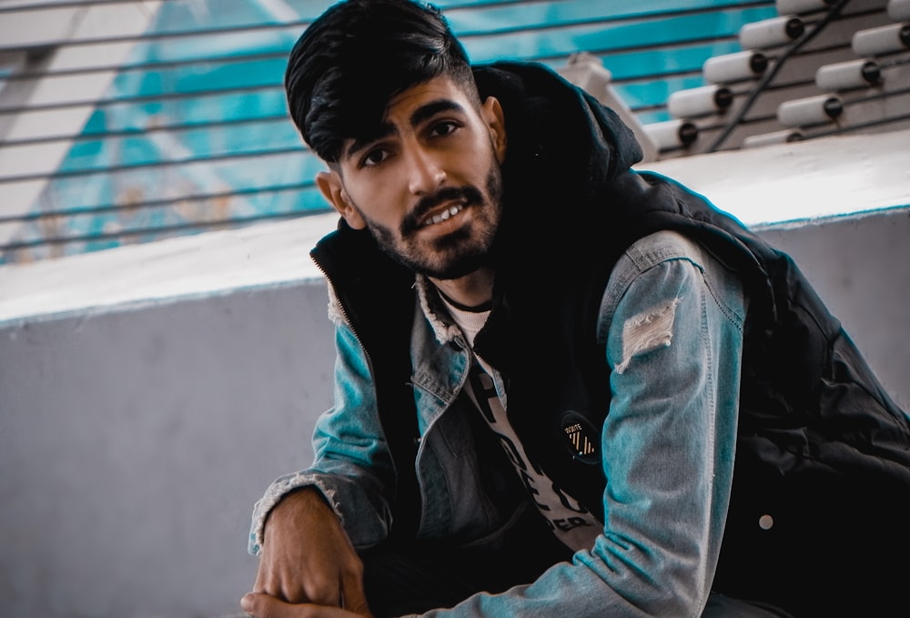 man in blue denim jacket sitting on white concrete bench