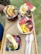 Three acai bowls are garnished with fresh slices of banana, watermelon, orange, strawberries, blueberries, and chocolate chips. The bowls are set on a wooden tray, accompanied by two wooden spoons, suggesting a colorful, healthy, and appetizing presentation.