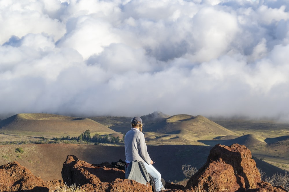 man and woman sitting on rock formation under white clouds during daytime