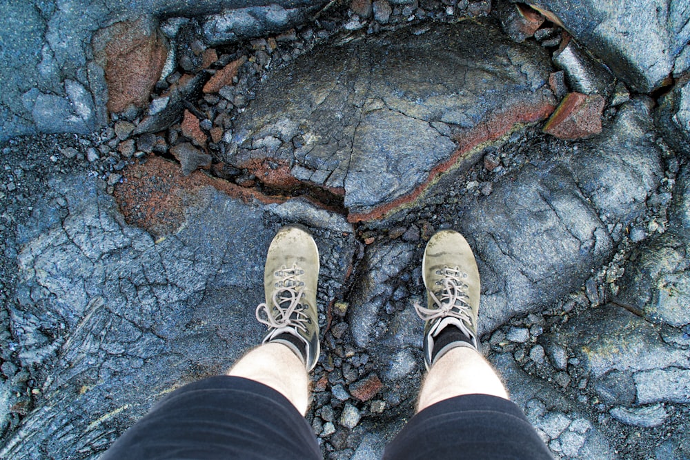 Persona con pantalones cortos negros y zapatillas blancas de pie en un suelo rocoso