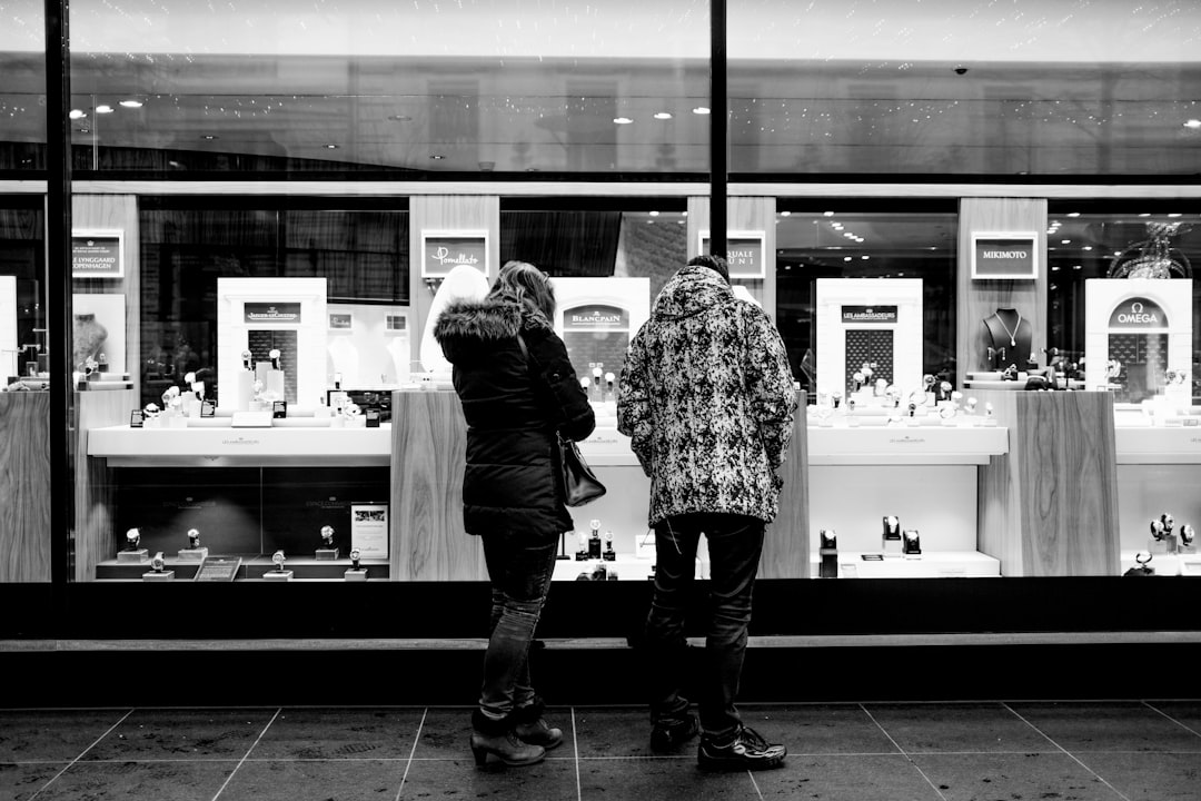 grayscale photo of 2 women standing in front of glass window
