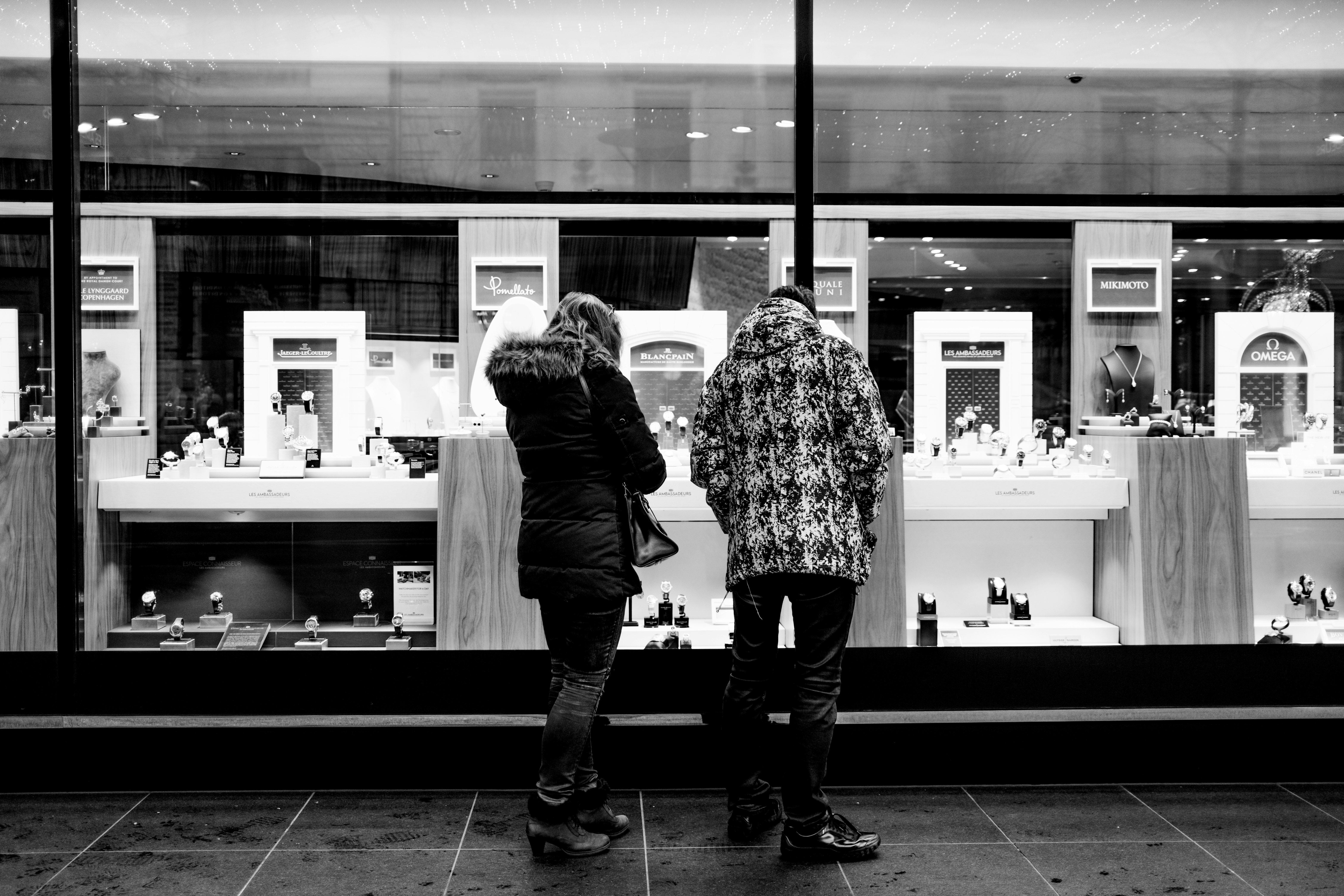 grayscale photo of 2 women standing in front of glass window