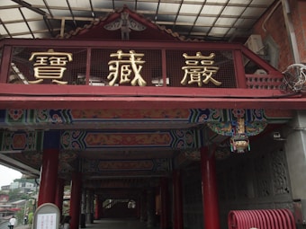 An ornate entrance with traditional Chinese architectural elements, decorated with colorful patterns and bold red columns. The structure features large gold Chinese characters against a contrasting deep red background. The ceiling is intricately painted with vibrant designs, adding to the cultural authenticity of the site.
