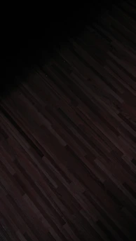 A dark, patterned wooden floor with subtle linear designs running horizontally. The lighting is dim, casting shadows that create a moody effect.