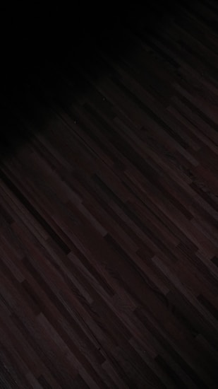 A dark, patterned wooden floor with subtle linear designs running horizontally. The lighting is dim, casting shadows that create a moody effect.