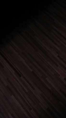 A dark, patterned wooden floor with subtle linear designs running horizontally. The lighting is dim, casting shadows that create a moody effect.