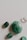 A collection of polished stones displayed on a smooth, light-colored surface. The stones vary in size and shape, with the most prominent being an oval-shaped green stone. Other stones include smaller green and clear stones, each with a shiny, glossy finish.
