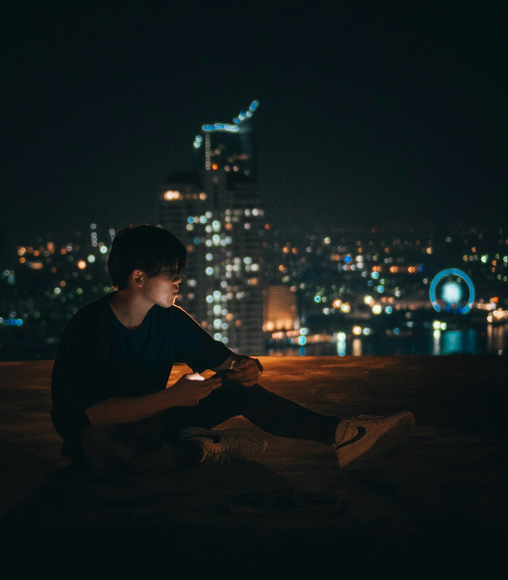 man in black crew neck t-shirt sitting on brown wooden table during nighttime