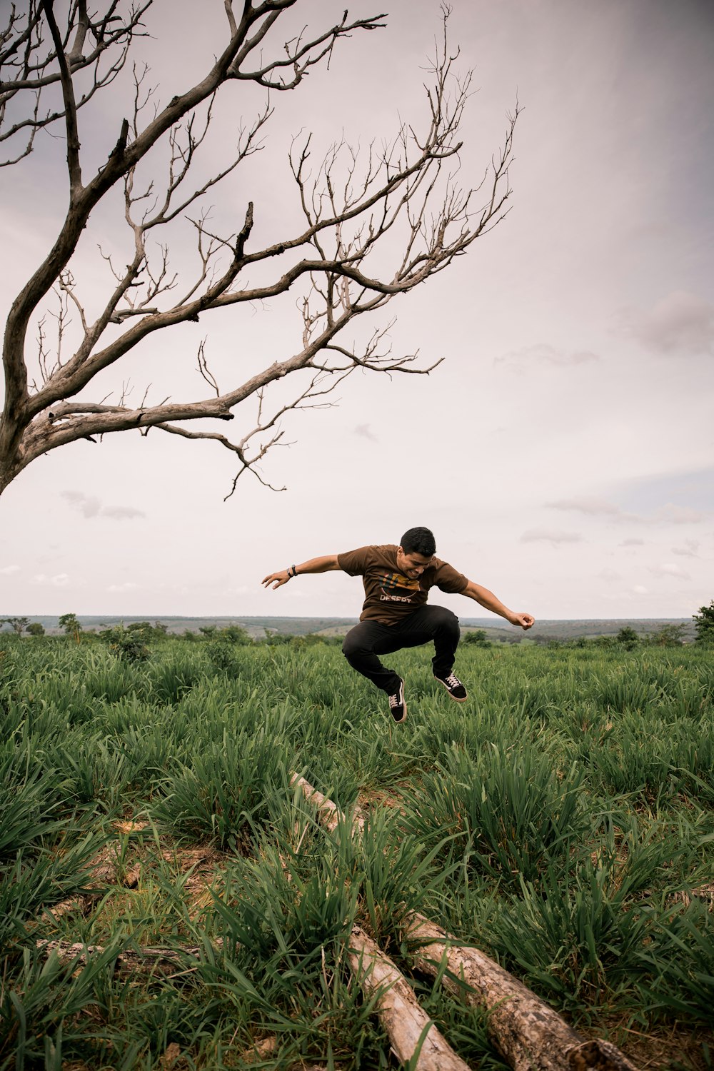 homme en chemise noire sautant sur le champ d’herbe verte pendant la journée