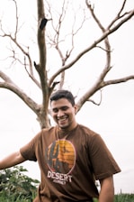man in brown crew neck t-shirt standing beside bare tree during daytime