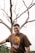 man in brown crew neck t-shirt standing beside bare tree during daytime