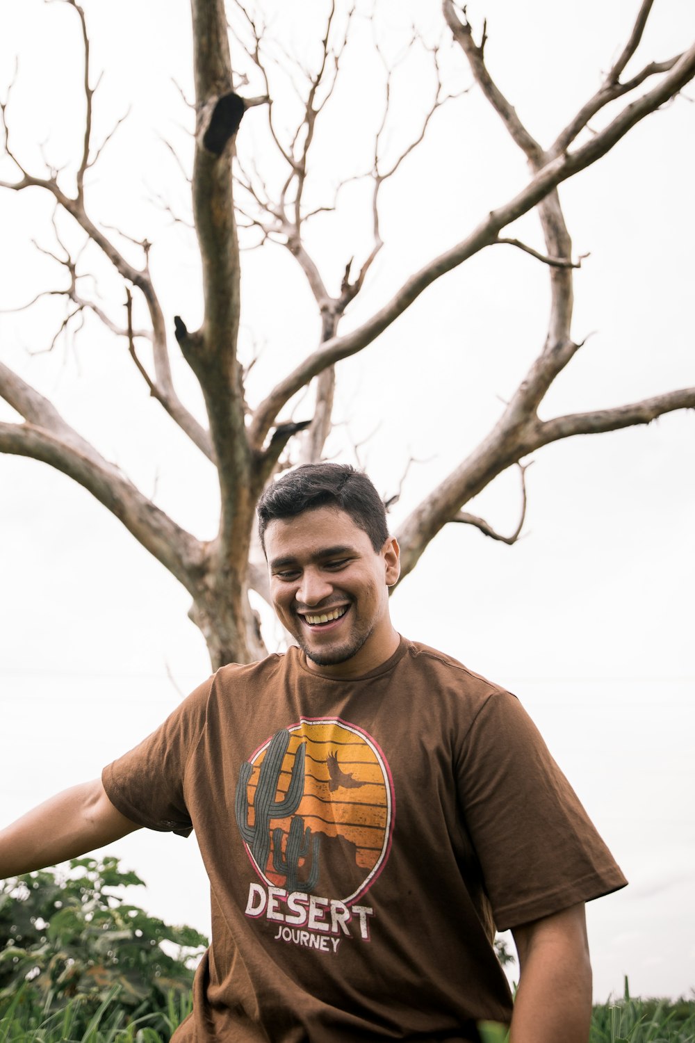 Mann im braunen Rundhals-T-Shirt steht tagsüber neben einem kahlen Baum