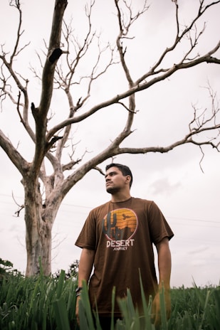 man in gray crew neck t-shirt standing beside bare tree during daytime