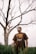 man in gray crew neck t-shirt standing beside bare tree during daytime