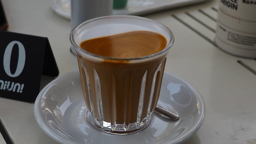 brown liquid in clear glass mug on white ceramic saucer