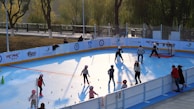 A group of children learning roller hockey skills on a smooth outdoor rink under a clear sky