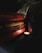 A stack of books is arranged on a dark surface, with titles including 'Harry Potter,' 'The Secret,' and 'My Experiments with Truth.' The dimly lit scene is softened by a small, glowing candle nearby and a green plant draping over from above, casting shadows and adding a cozy atmosphere.