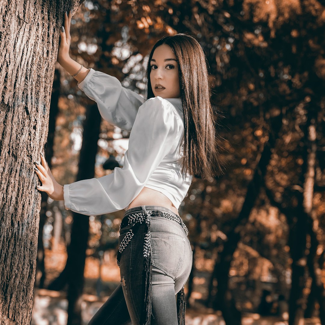 woman in white long sleeve shirt and black pants sitting on tree trunk during daytime