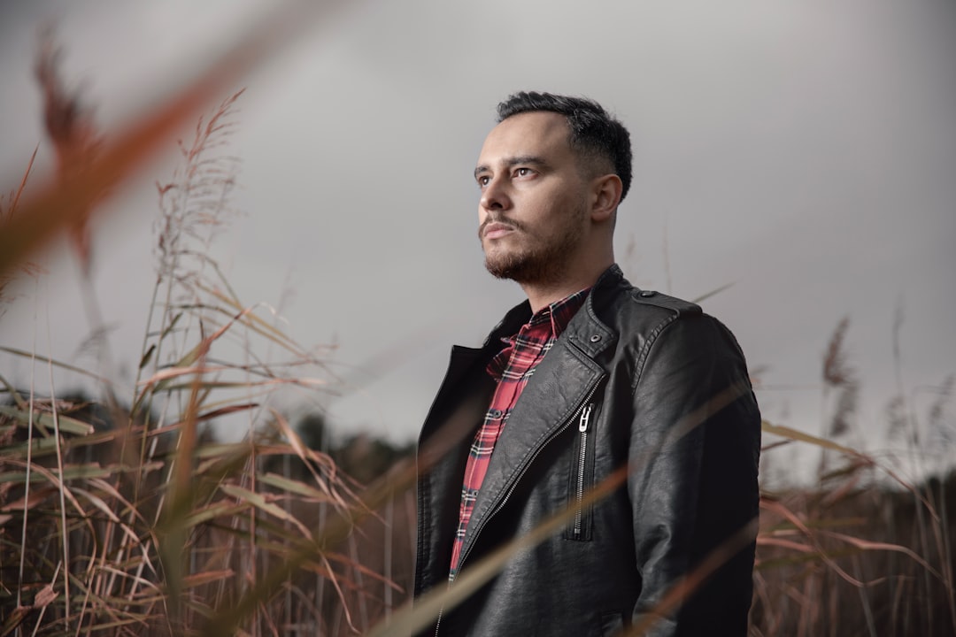man in black leather jacket standing on brown grass field during daytime