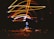 Bright streaks of light in shades of orange and blue create a dynamic pattern against a dark background. At the center, a glowing object, resembling a lamp or bulb, emits a vibrant blue hue. The light patterns loop and swirl above and around this central object.