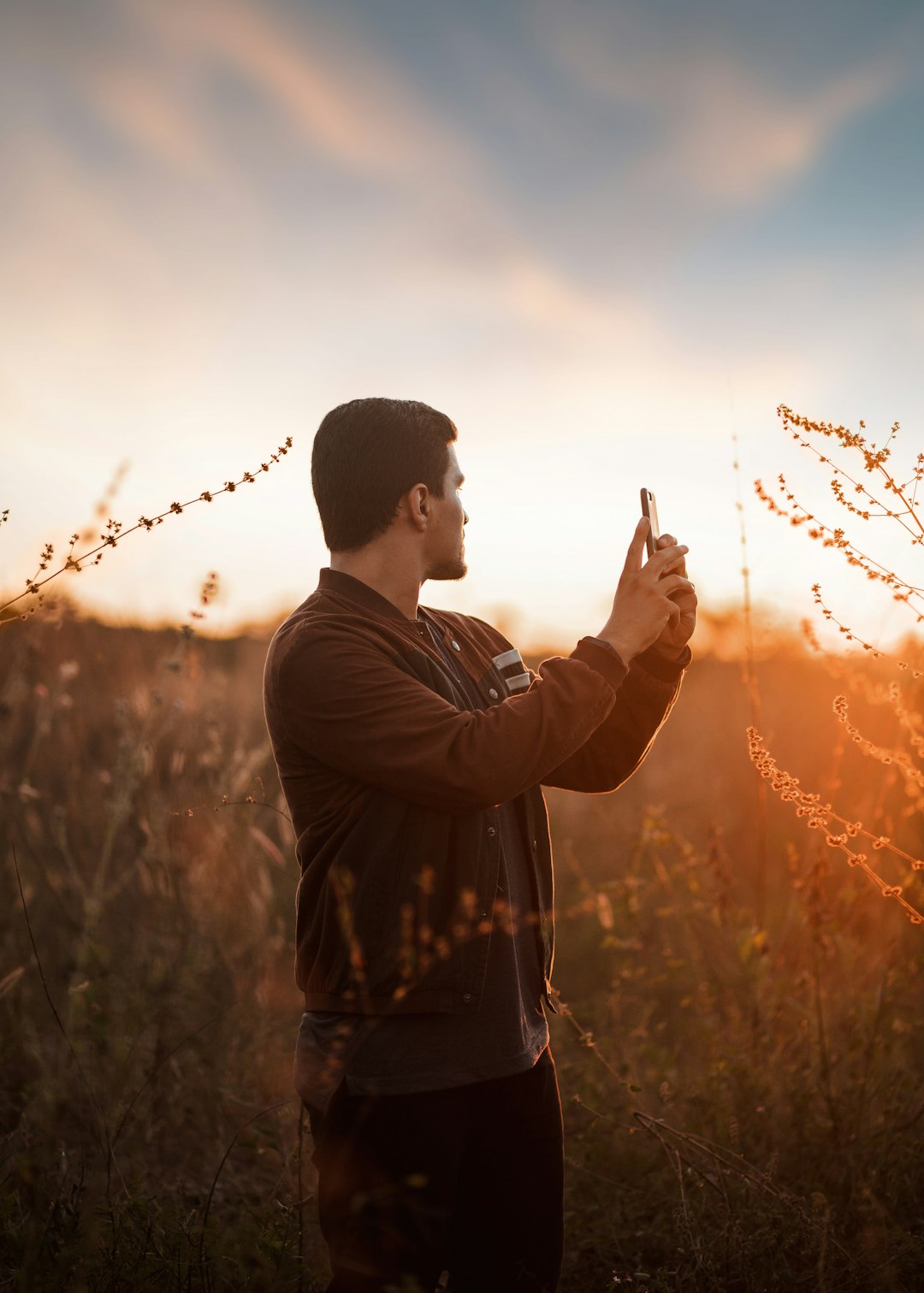 man in black jacket standing on grass field during sunset