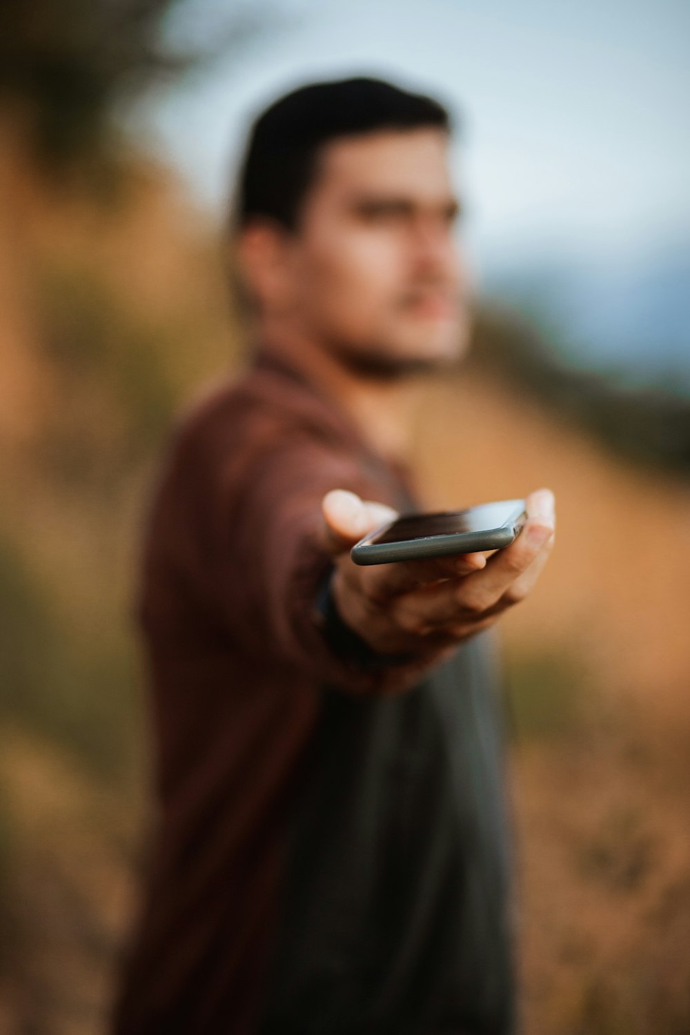 黒いスマートフォンを持つ茶色のセーターの男性