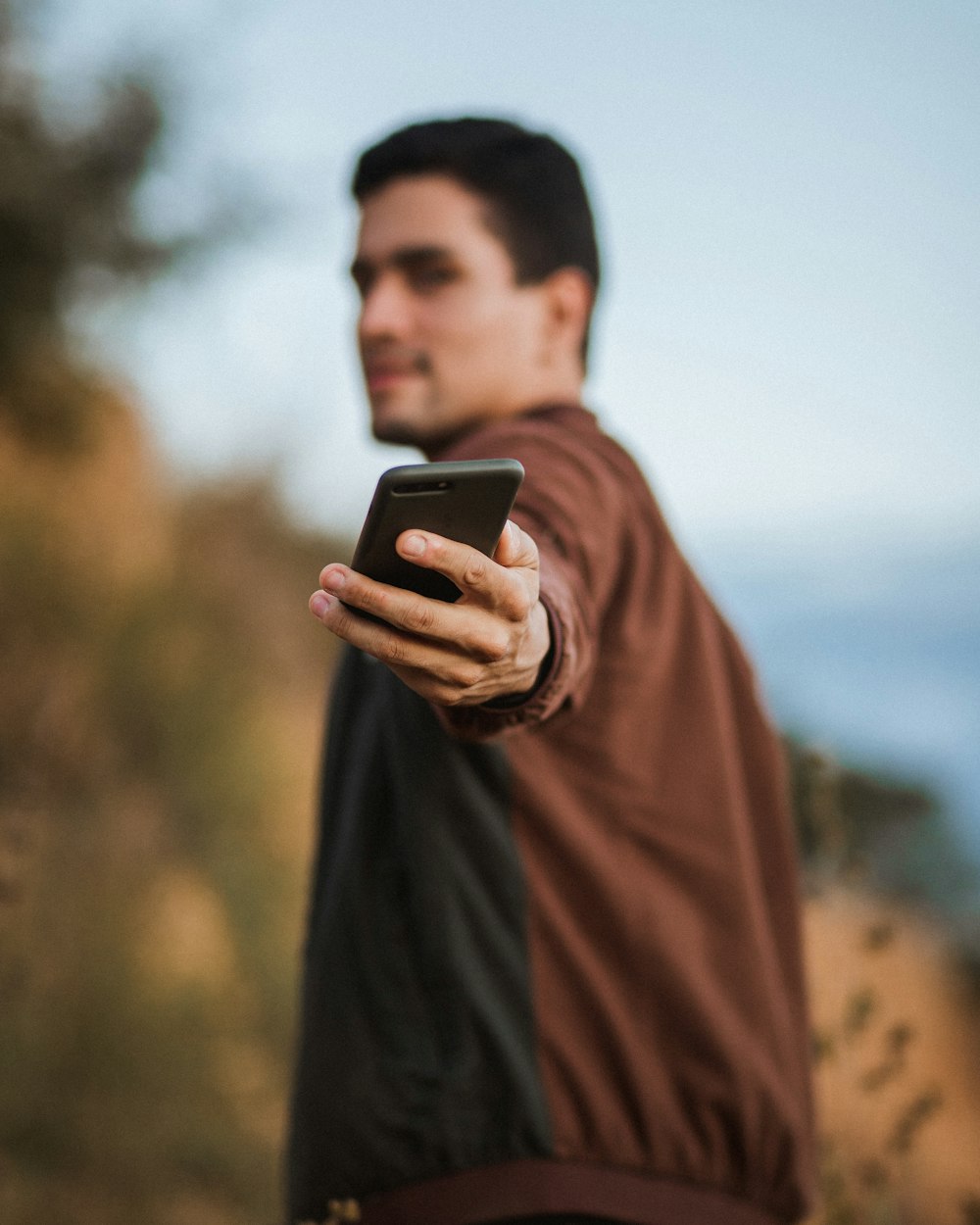 黒いスマートフォンを持つ茶色の長袖シャツを着た男性