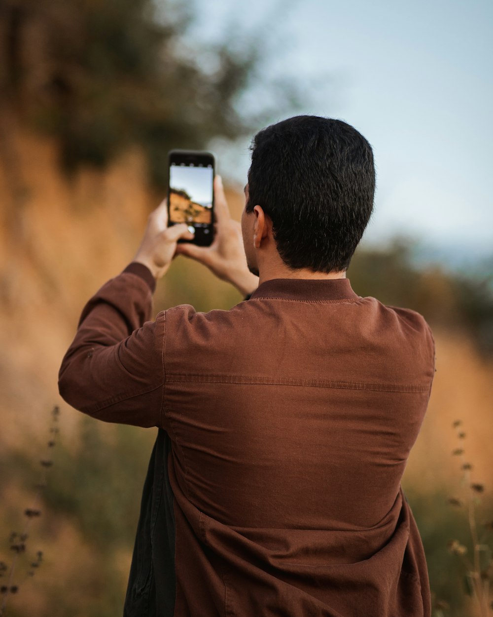 uomo in camicia a maniche lunghe marrone che scatta foto del tramonto