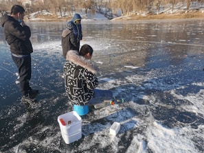 A winter scene showing ice fishing with students gathered around a hole in the frozen lake.
