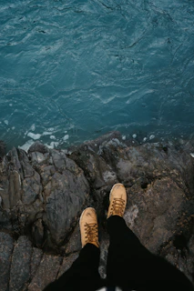 person in black pants and brown shoes standing on rocky cliff