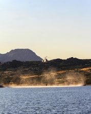A helicopter hovering above lush green hills with a river winding below.