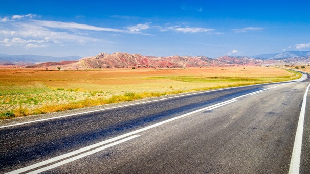 A freshly paved asphalt road winding through a rural landscape under a clear blue sky.