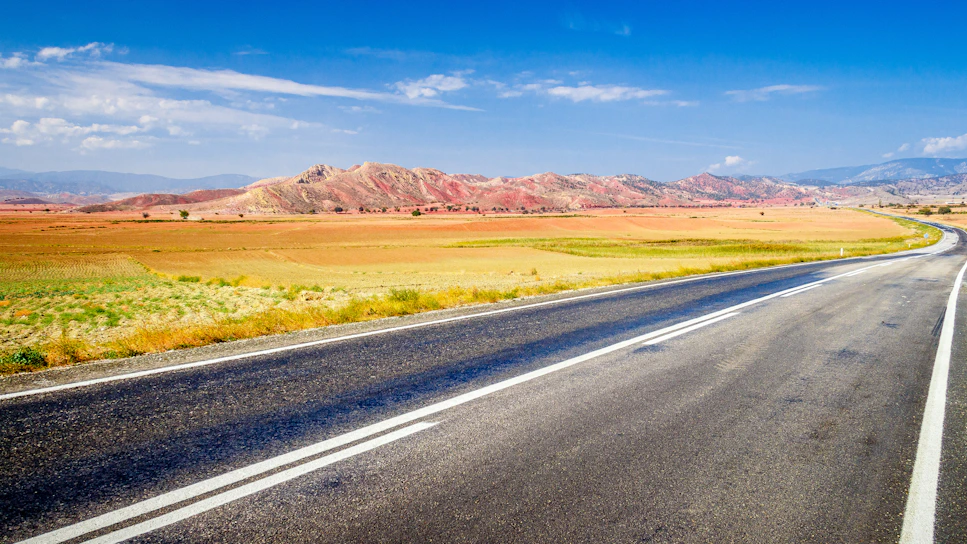 A freshly paved asphalt road winding through a sunny landscape, showcasing smooth blacktop and clear lane markings.