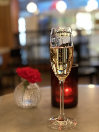 Close-up of a delicate glass of champagne resting on a polished wooden table beside a bouquet of fresh flowers.